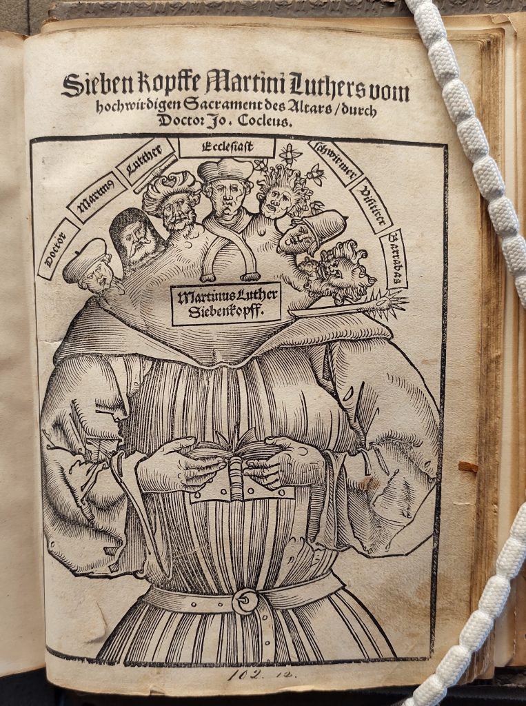 Title Page of a 16th century printed text featuring a large woodcut that shows Martin Luther with seven different heads, which have inscriptions next to it: 'Doctor', 'Martinus', 'Luther', 'Ecclesiast', 'Schwirmer', 'Visitirer' and 'Barrabast'.